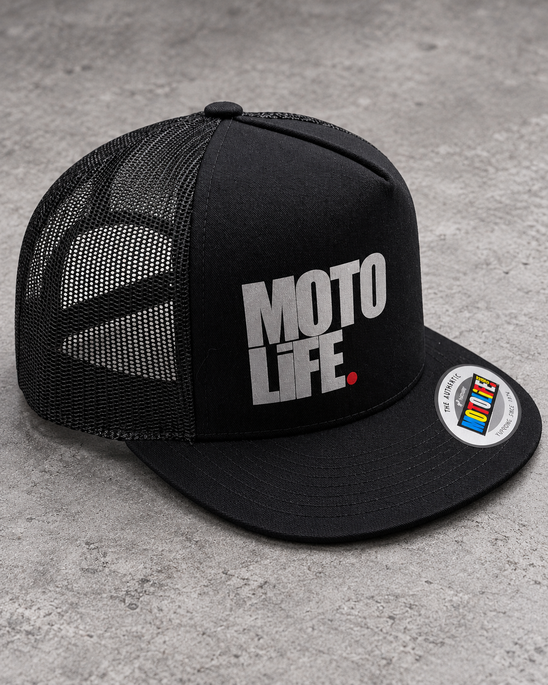 Black MOTOLiFE mesh snapback on gray concrete, three-quarter front view with silver reflective stacked logo and red period.