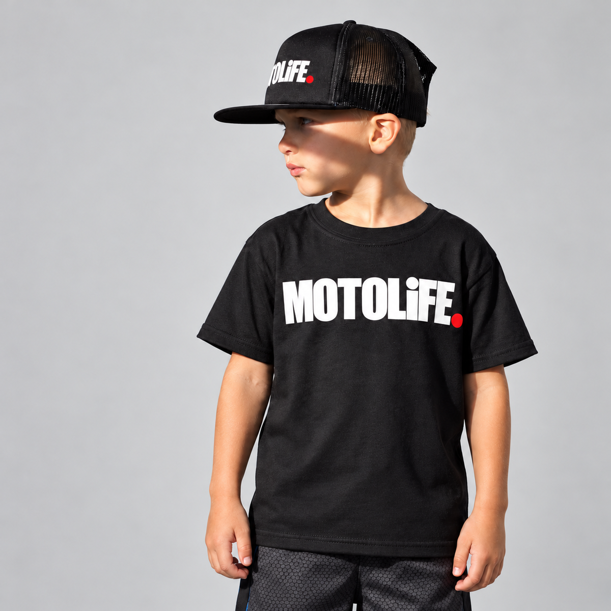 Black MOTOLiFE kids tee worn by a child in a gray studio setting; hat sold separately
