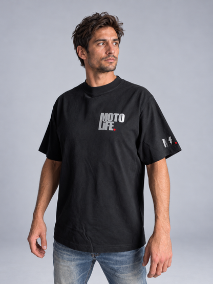 Black V2 short-sleeve tee on model with small stacked reflective left-chest logo, blue jeans and tan work shoes.